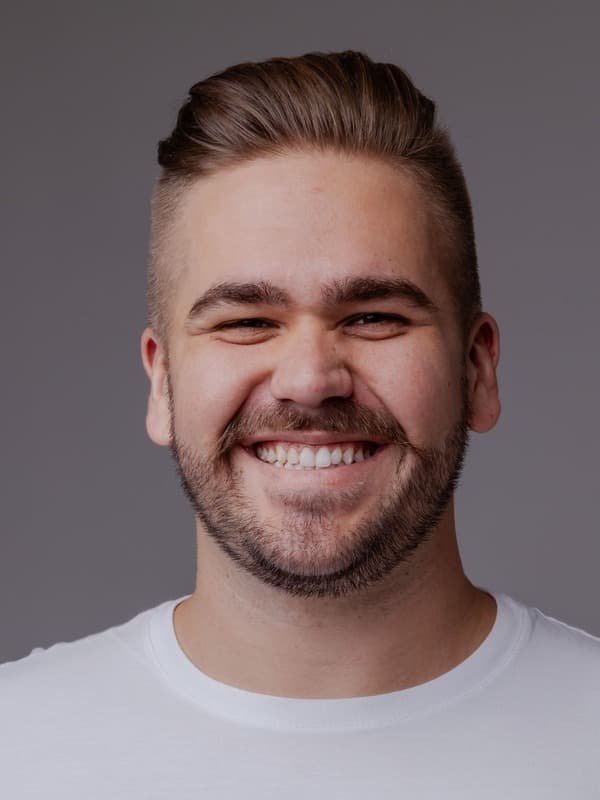 Matheus Fischer, sorrindo, camiseta branca, fundo cinza de estúdio